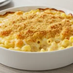 A golden, bubbly dish of old fashioned baked macaroni and cheese in a white ceramic baking dish on a rustic kitchen table."