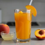 A glass jar filled with homemade peach nectar next to fresh peaches and lemon juice on a kitchen countertop.