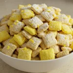 Lemon Muddy Buddies bowl on a modern kitchen countertop with fresh lemon zest and powdered sugar.