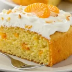 Close-up of a moist mandarin orange cake slice with creamy frosting and orange pieces.