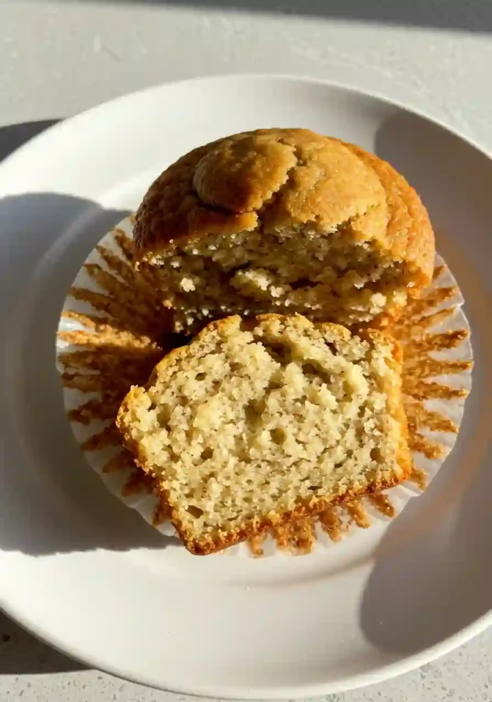 High-Protein cottage cheese banana muffins 6 One golden-yellow cottage cheese banana muffin sliced in half on a white plate, showing the soft and moist crumb inside.