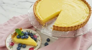 A perfect slice of homemade lemon tart on a white plate, showing the thick yellow curd filling and buttery crust, with a dusting of powdered sugar.